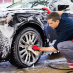 Man worker washing car’s alloy wheels on a car wash